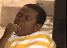 a young boy in a yellow and white striped shirt eating a sandwich